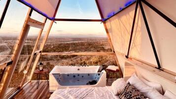 A tented accommodation with a bed, a bathtub, and a view of the landscape.