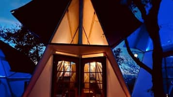 A tent with a triangular roof and a central door, surrounded by trees.