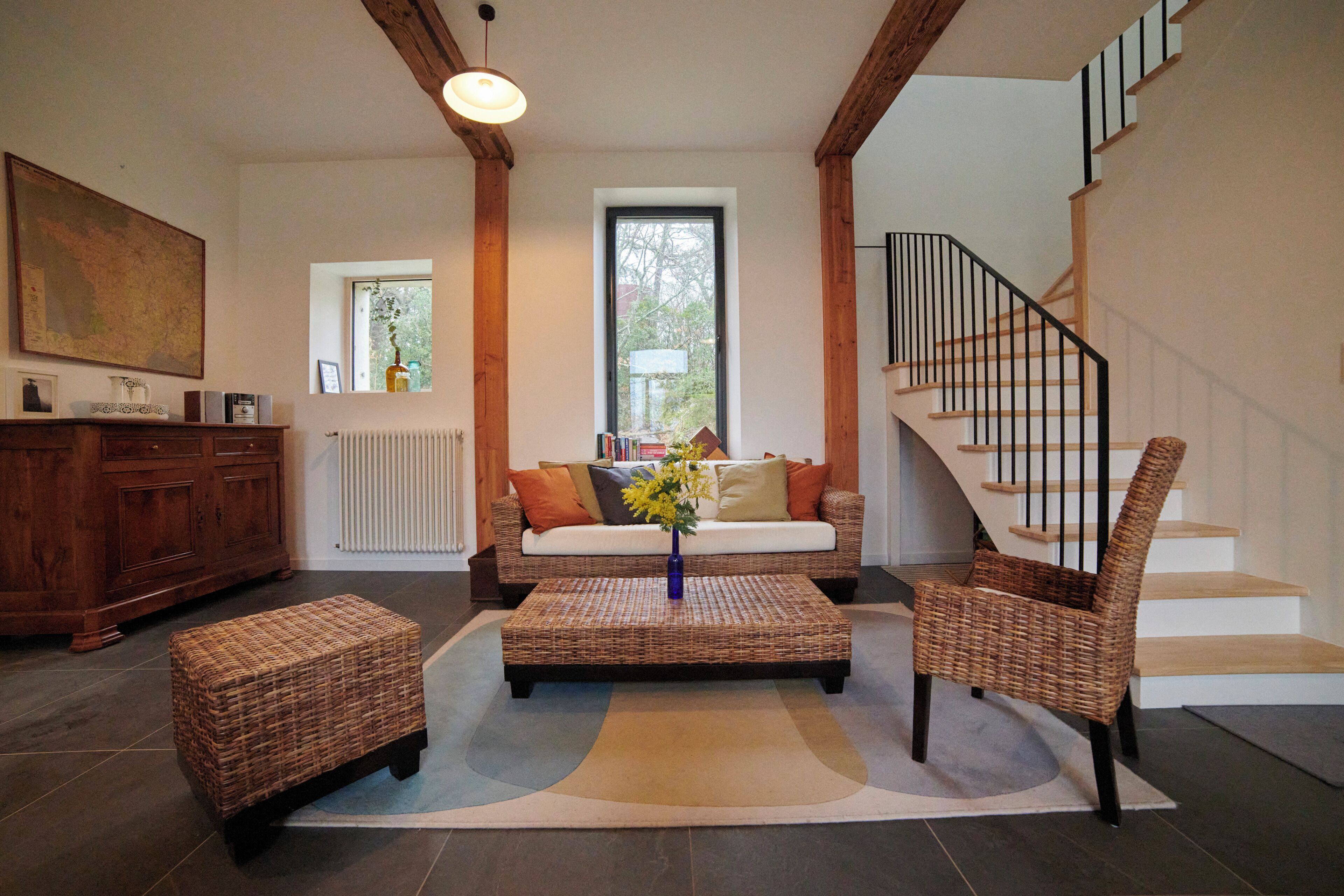 A living room with a sofa, a coffee table, a wicker ottoman, a chair, a staircase, and a wooden cabinet.