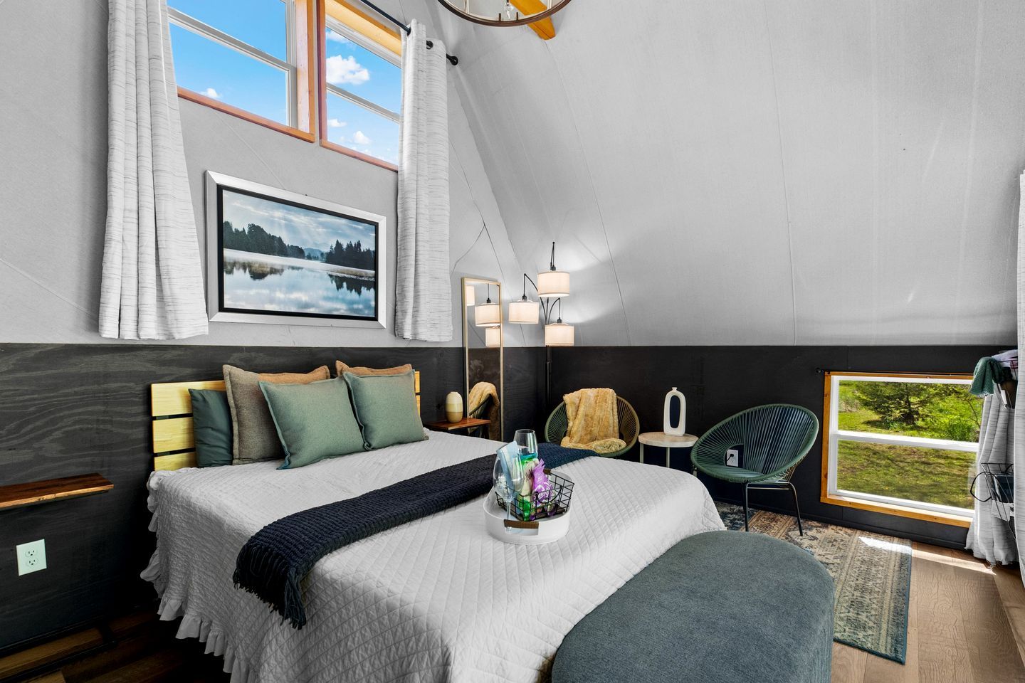 A bedroom with a bed, bedside tables, a window with a view, a hanging light fixture, and a mirror.