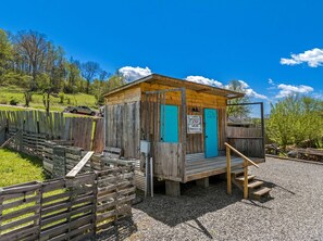 Una cabaña de madera con puerta azul, un porche pequeño y un letrero que indica que es baño y sanitario.