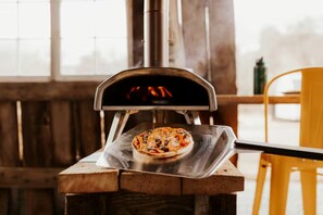 Un four à pizza avec une pizza à l’intérieur, une table en bois et une chaise jaune.