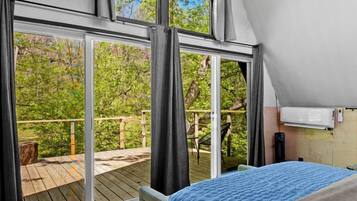 A bedroom with a large bed, a chandelier, a view through a sliding door to an outdoor deck, and a ceiling fan.