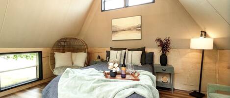 A cozy bedroom with a bed, bedside tables, a hanging light fixture, and a window.