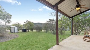 En overdækket terrasse med beton gulv, loftventilator og en gyngestol.