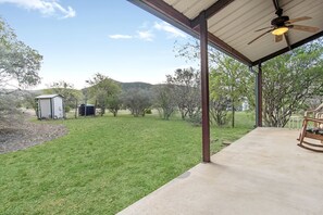 A covered patio with a concrete floor, a ceiling fan, and a rocking chair. - Charming Hill Country Escape with Scenic Views & Outdoor Spaces in Concan, Texas (Concan)