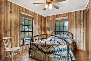 A wooden-paneled room with a bed, a chair, and a ceiling fan. - Charming Hill Country Escape with Scenic Views & Outdoor Spaces in Concan, Texas (Concan)