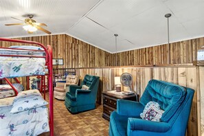 A room with bunk beds, a blue armchair, a wooden wall, and a ceiling fan. - Charming Hill Country Escape with Scenic Views & Outdoor Spaces in Concan, Texas (Concan)