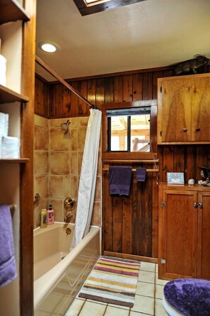 A bathroom with wooden paneling, a bathtub, a window, and a striped rug.