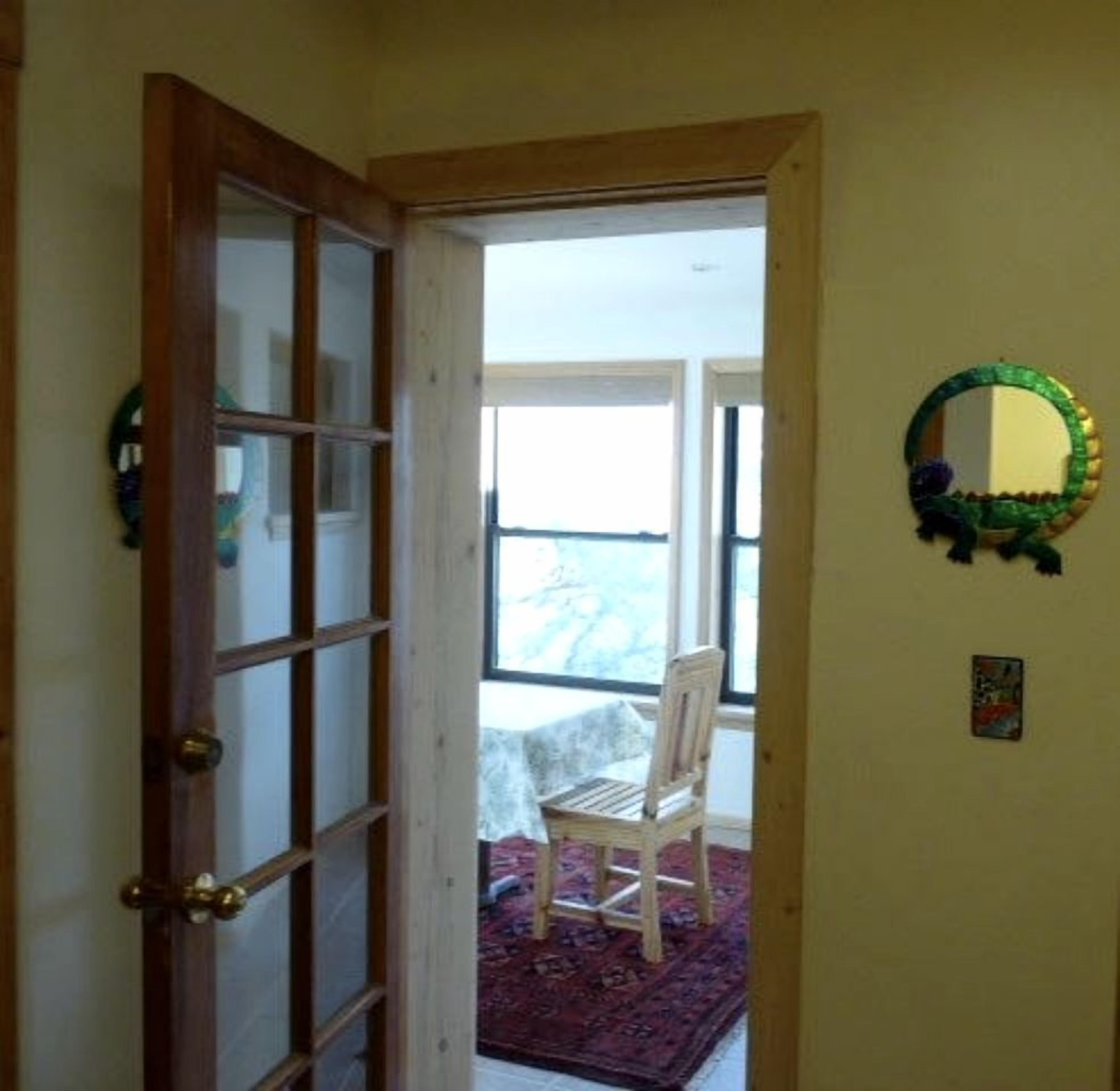 Una habitación con puerta de madera, una silla, un tapete y un espejo en la pared.