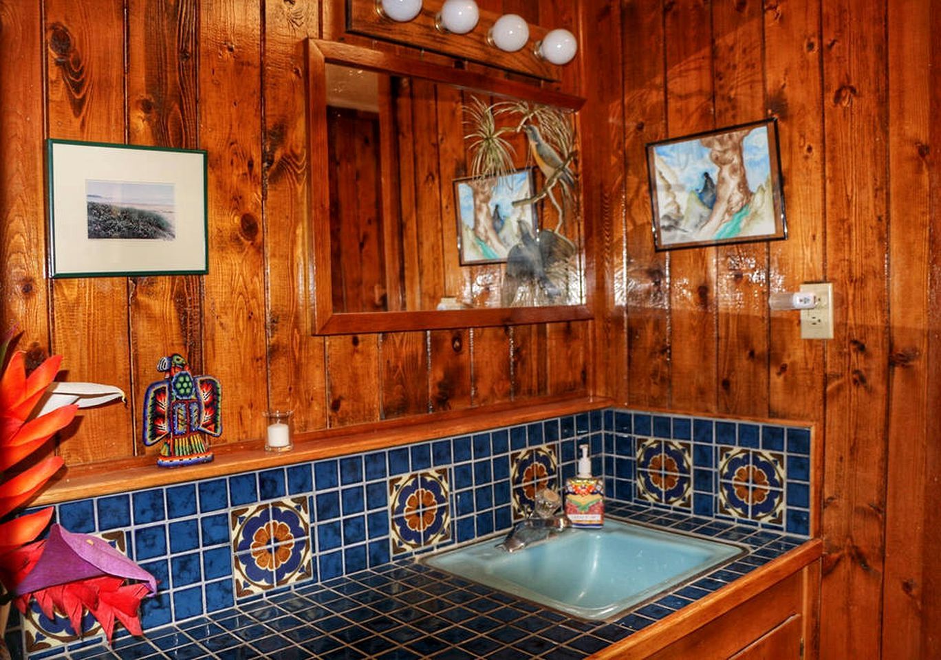 Un baño de madera con lavamanos de azulejos azules, cuadros enmarcados y pared de madera.