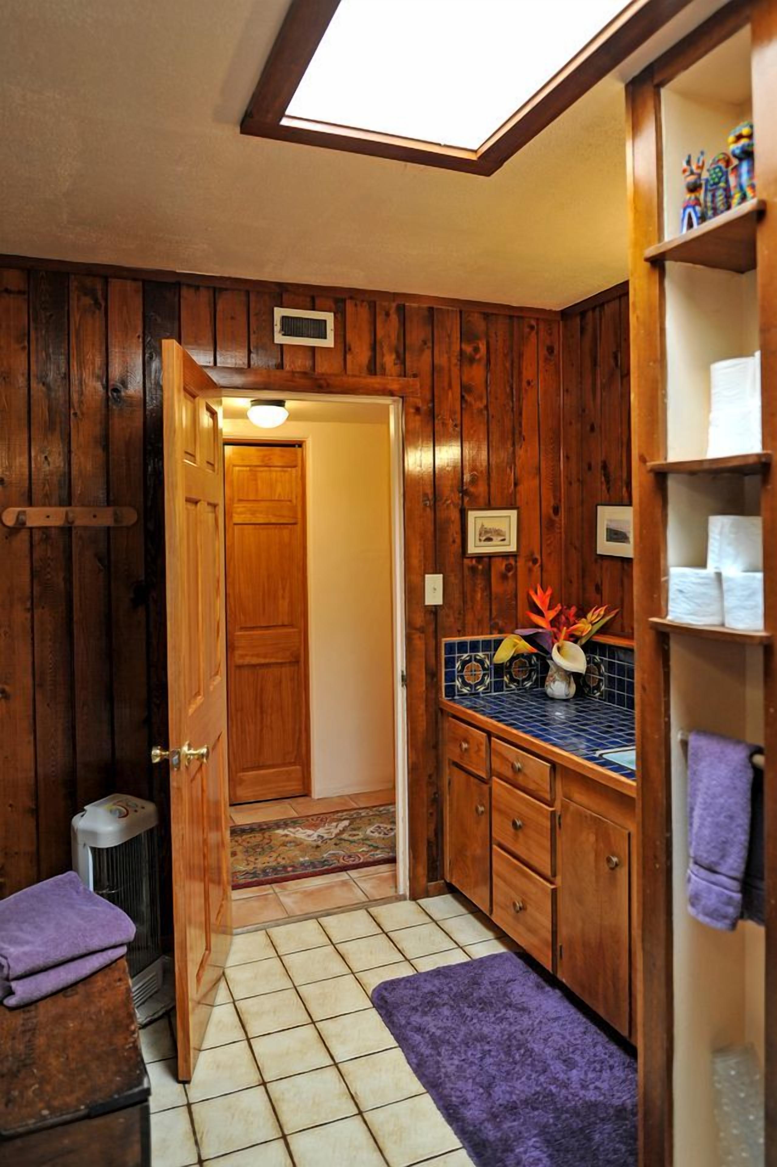 Un baño con paneles de madera, un tragaluz, un perchero y un pequeño estante con artículos de aseo.