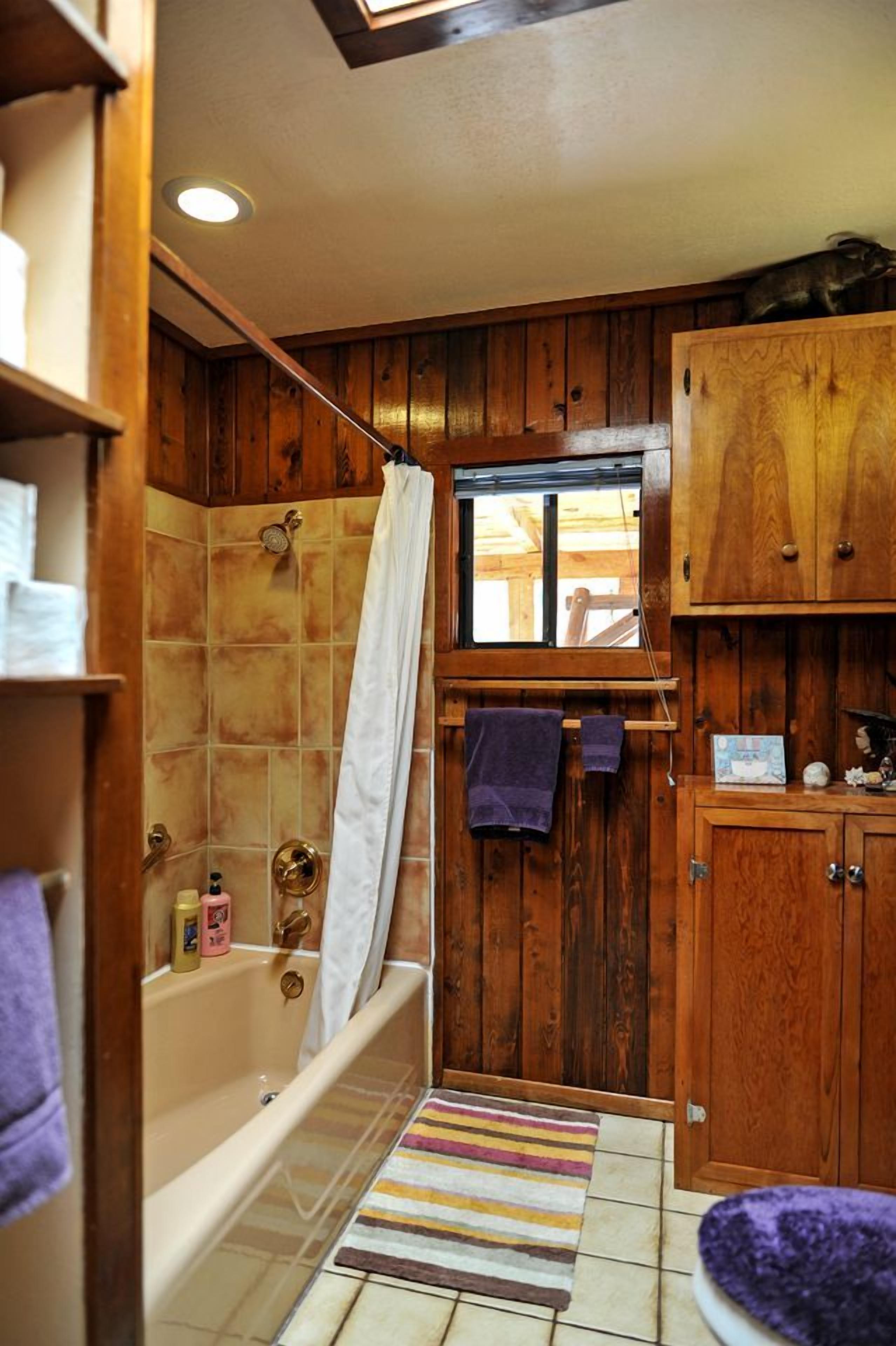 A bathroom with wooden paneling, a bathtub, a window, and a striped rug.