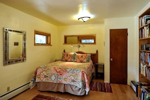 A bedroom with a bed, a bookshelf, a door, a mirror, and a window.