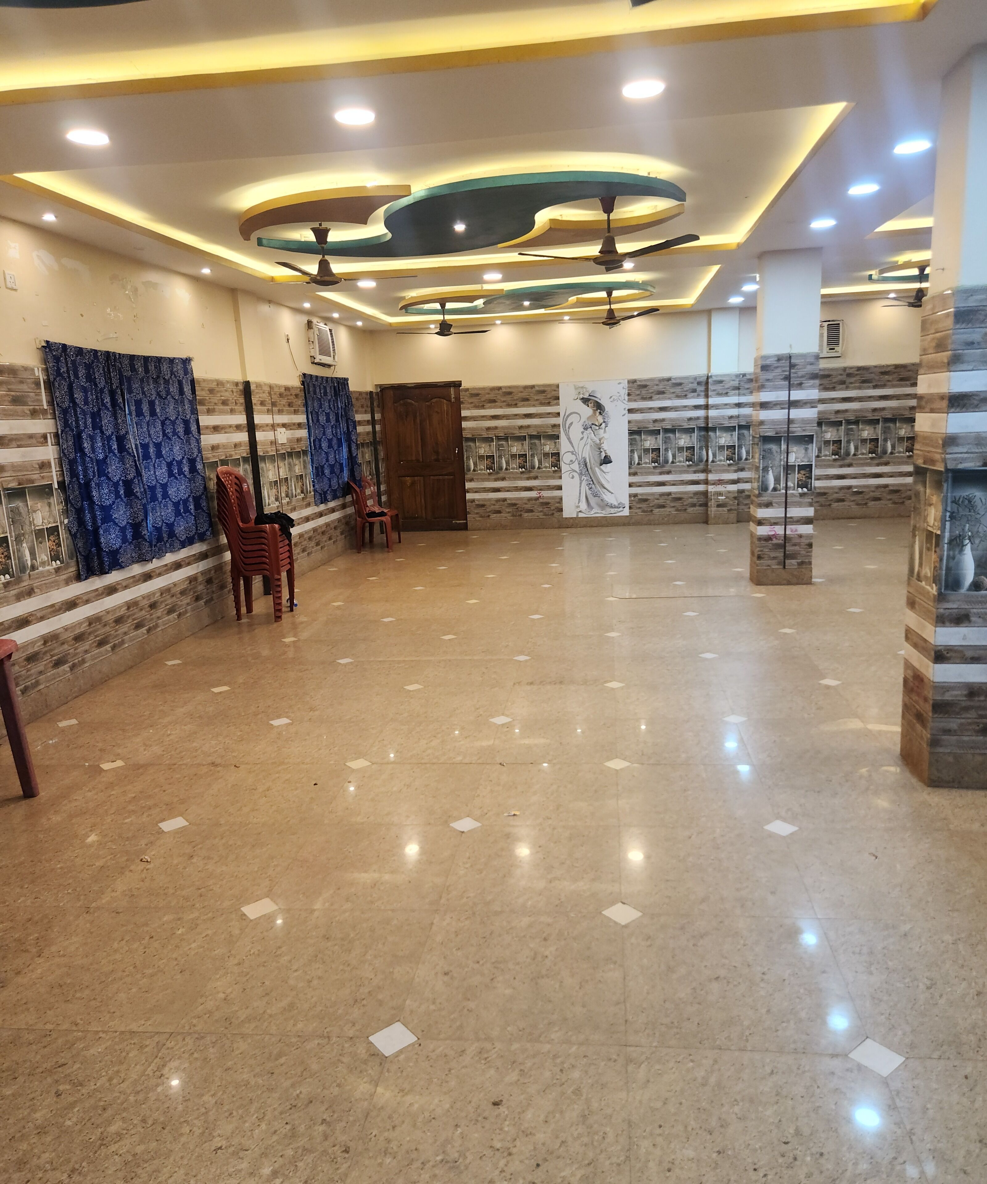 Um hall amplo com piso de mármore polido, ventiladores de teto, iluminação embutida e um grande mural na parede.