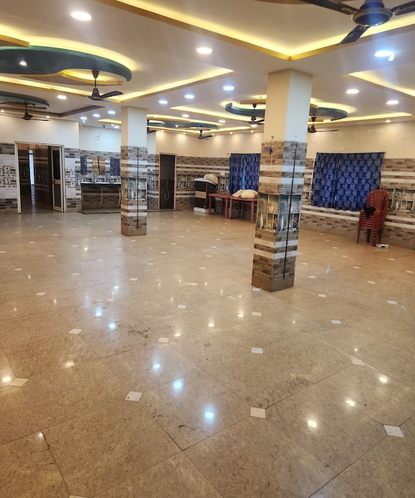 Un hall d’entrée spacieux doté d’un sol en marbre poli, de ventilateurs de plafond, d’un éclairage encastré et d’un coin salon avec une table et des chaises.