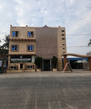 Un hôtel à la façade ornée de motifs, une enseigne indiquant « Swayamsiddha Hotel & Restaurant », et une entrée fermée par un portail.
