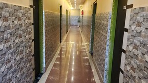 A hotel corridor with a polished floor, stone-patterned walls, and green doors. - Swayamsiddha Continental (Kendrapara)
