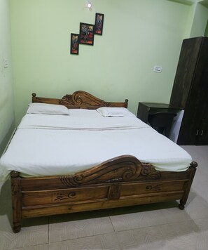 A wooden bed with a headboard, a bedside table, and a wardrobe in a room with light green walls.