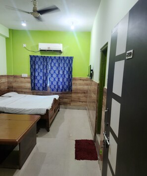 A room with a bed, a desk, a ceiling fan, an air conditioning unit, and a green wall.