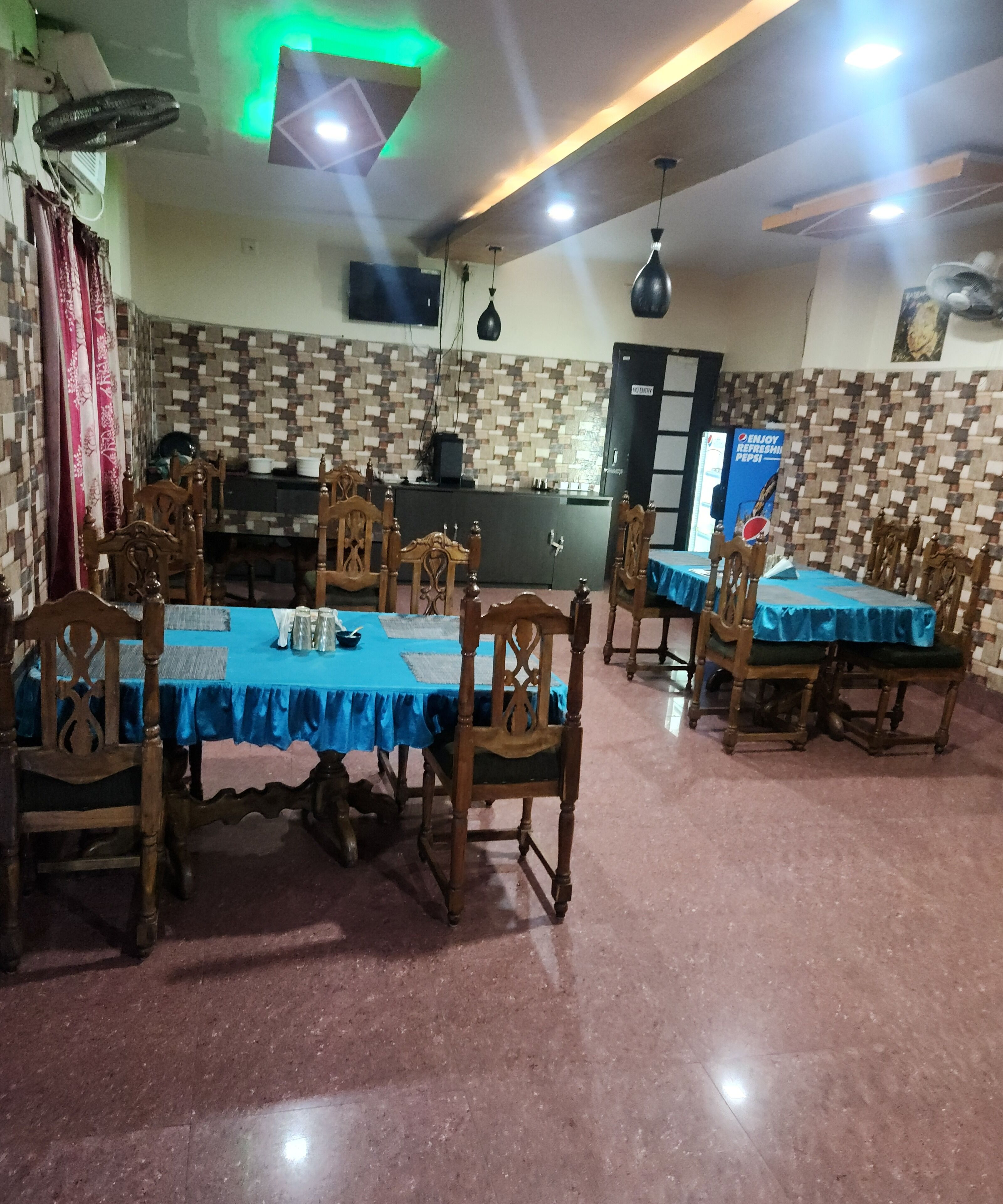 Een restaurant met een betegelde muur, houten stoelen, een tafel met een blauw tafelkleed en een balie met een Pepsi-reclame.