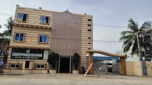 Un hotel con fachada estampada, un letrero que dice 'Swayamsiddha Hotel & Restaurant' y una entrada porticada.