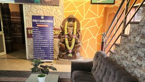 A hotel lobby with a sofa, a small table with a plant, a poster with a menu, and a statue of an elephant. - Swayamsiddha Continental (Kendrapara)