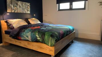Una cama con una colcha estampada con hojas, un cabecero de madera y una obra de arte en la pared superior.