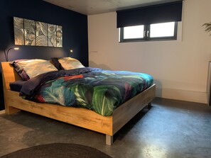 Ein Bett mit Bettdecke mit Blätermotiv, ein Holzkopfteil und ein Wandbild darüber.