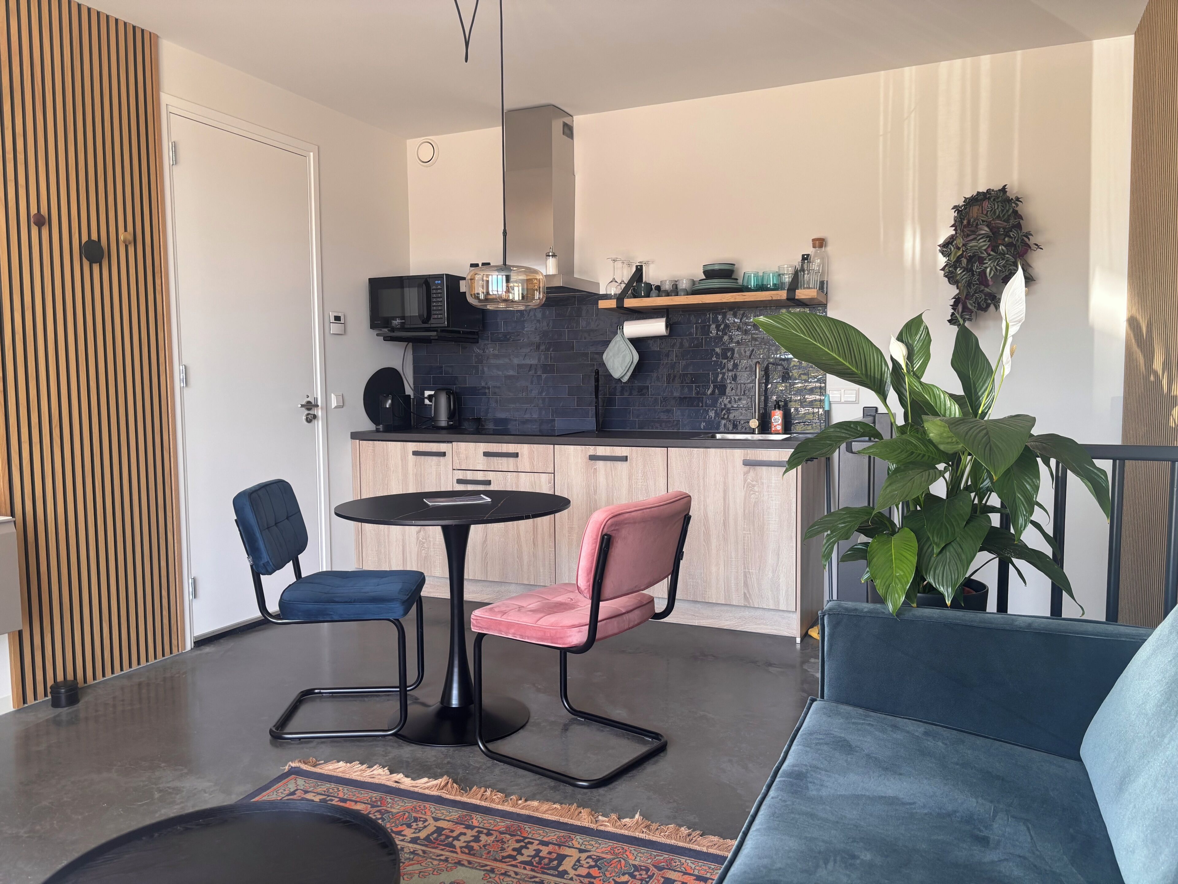 Une cuisine moderne avec un plan de travail noir, un four à micro-ondes et une machine à café. On y trouve également un coin repas avec une table ronde et deux chaises.