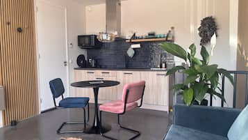 Une cuisine moderne avec un plan de travail noir, un four à micro-ondes et une machine à café. On y trouve également un coin repas avec une table ronde et deux chaises.