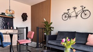 Ett modernt vardagsrum med en soffa, en fåtölj, ett litet bord, en matta, en krukväxt och en cykel som hänger på väggen.