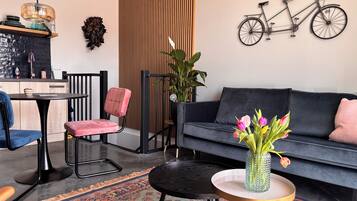 Un salon moderne comprenant un canapé, un fauteuil, une petite table, un tapis, une plante en pot et un vélo fixé au mur.