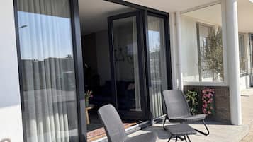 Un balcon avec deux chaises, une porte-fenêtre coulissante et une vue sur l’intérieur.