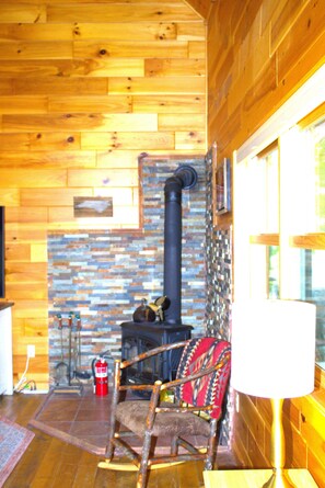 A wooden interior with a fireplace, a rocking chair, and a window. - Tracey's Gem Cabin Franklin, NC (Franklin)