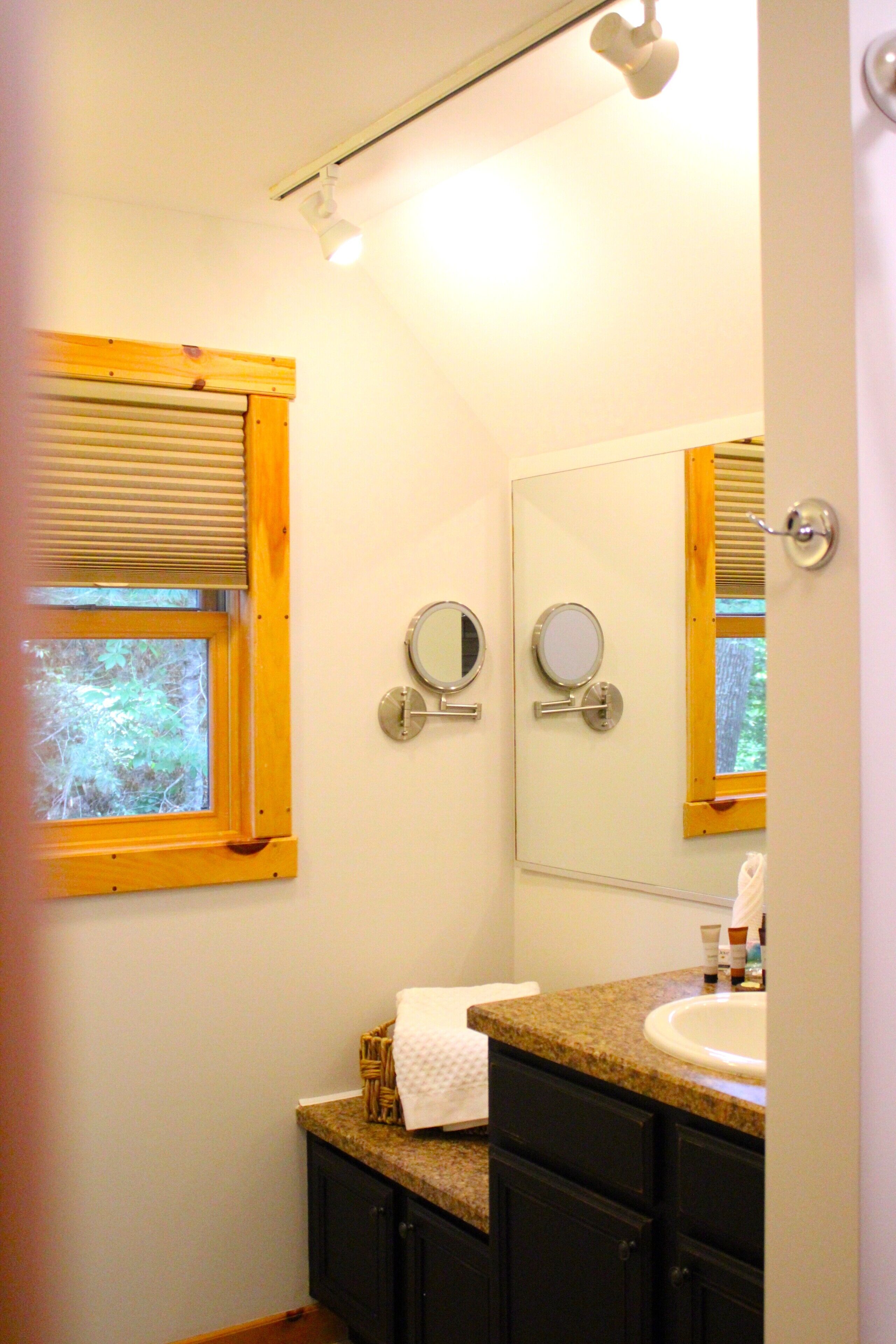 A bathroom with a window, two mirrors, a sink, and a towel.