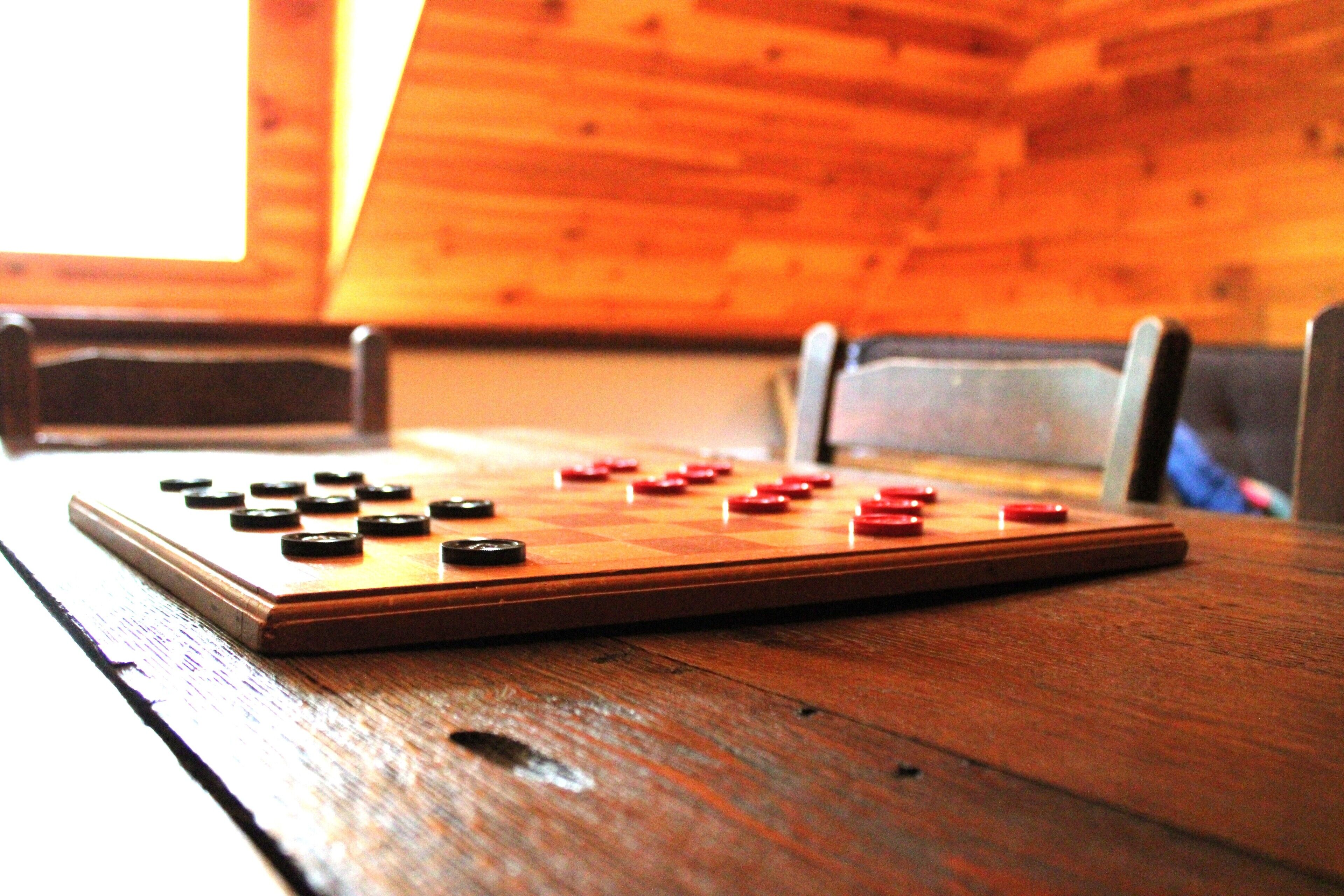 Una mesa de madera con un tablero de juego de cuadros y piezas, ubicada en una habitación con paredes y techo inclinados de madera.
