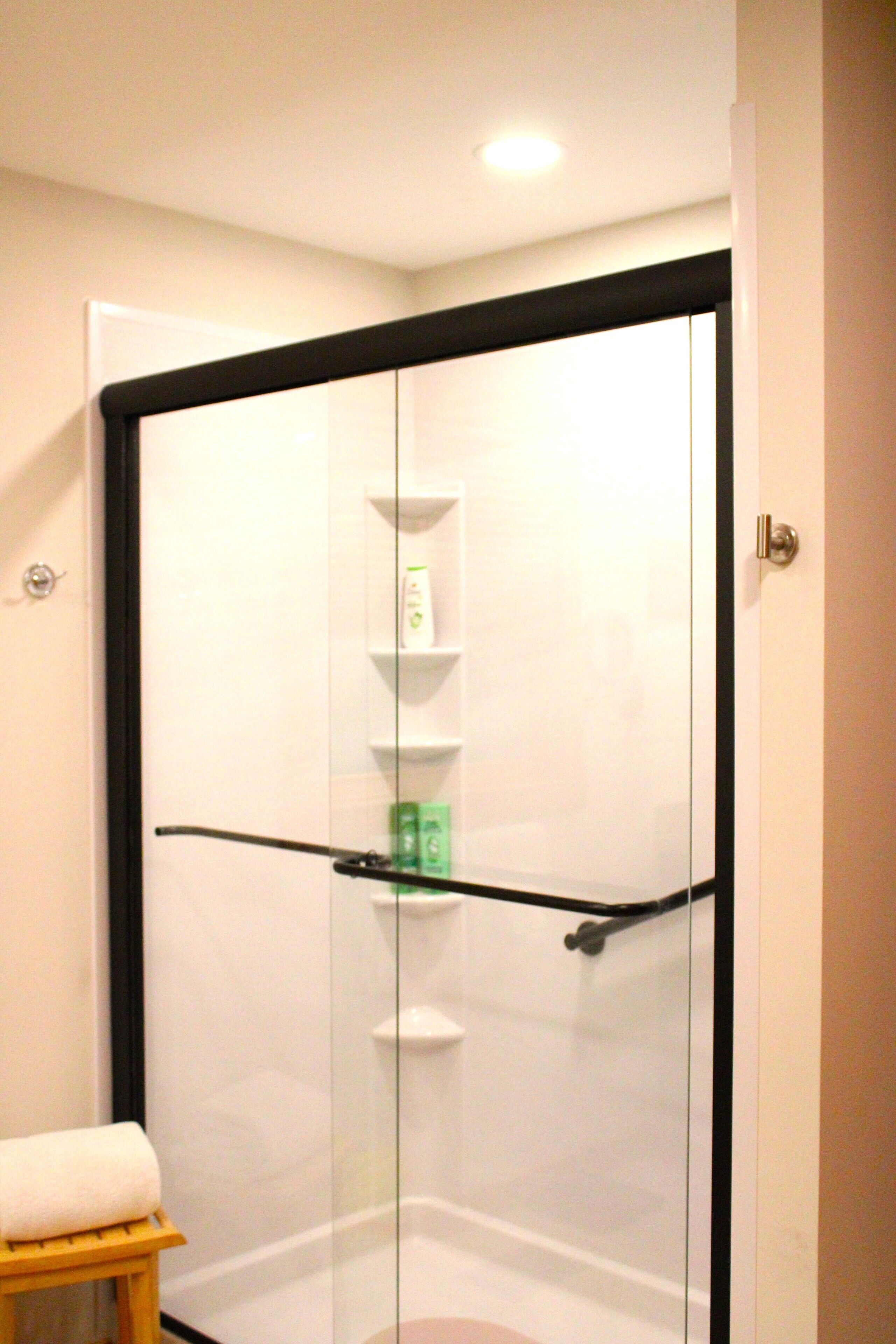 Une douche fermée par des parois en verre, avec un porte-serviettes et une étagère pour les articles de toilette.