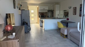 Une cuisine moderne avec un îlot central, un coin repas avec une chaise jaune et un espace salon avec un canapé.