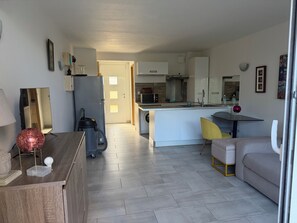 Ett modernt kök med en köksö i mitten, en matplats med en gul stol och ett vardagsrum med en soffa.