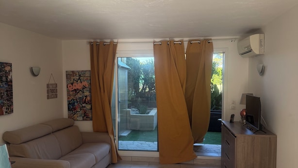 Un salon comprenant un canapé, une table basse, un téléviseur posé sur un meuble en bois et une porte-fenêtre coulissante donnant sur un espace extérieur.
