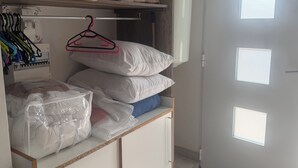 Une petite pièce comprenant un lit, une armoire, une petite étagère avec des vêtements pliés et une porte avec des fenêtres.