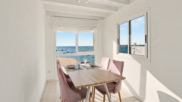A dining area with a view of the sea, a wooden table, and pink chairs. - B-rent Bluemarlin Boutique Sea View – Central Apartment with Stunning Ocean Views (Corralejo)