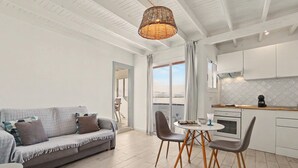 A modern living room with a sofa, chairs, a table, and a kitchen area with cabinets and a stove. - B-rent Bluemarlin Boutique Sea View – Central Apartment with Stunning Ocean Views (Corralejo)