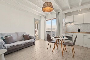 Un salon moderne comprenant un canapé, des fauteuils, une table et un coin cuisine avec des placards et une cuisinière.
