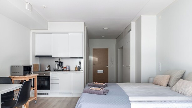 A compact hotel room with a kitchenette, a bed, a desk, and a chair.