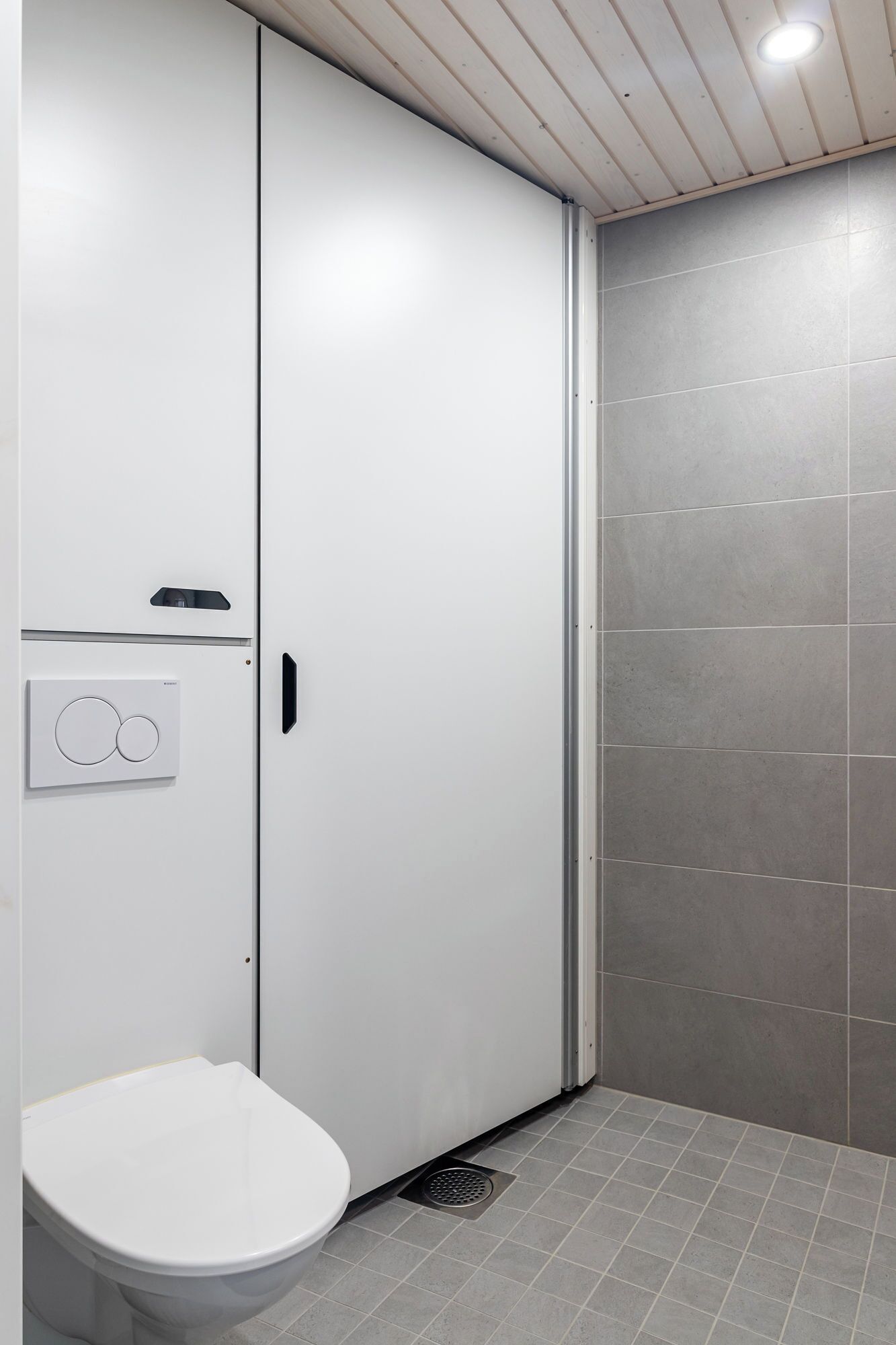 A modern bathroom with a toilet, a white cabinet, and a shower area.