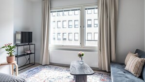A modern living room with a large window, a flat-screen TV, a small table with a vase, a sofa, and a radiator.