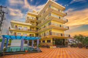 A multi-story hotel with balconies, a swimming pool, and a checkered pavement area. - DREAM BASANTI (Mandarmani)