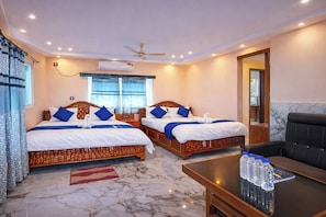 Une chambre d’hôtel avec deux lits, un ventilateur de plafond, un appareil de climatisation, un sol en marbre et une table avec des bouteilles d’eau.